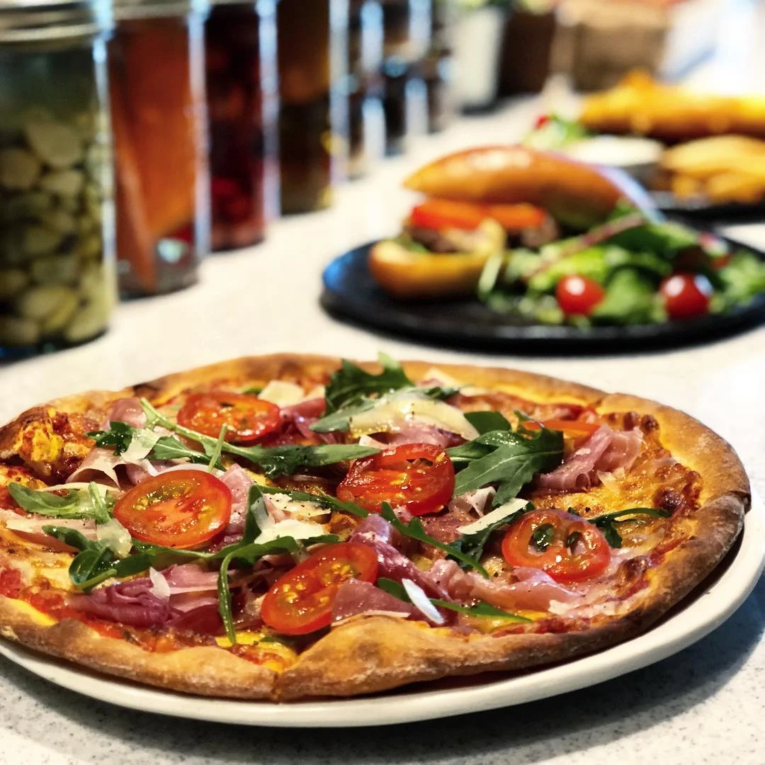 Pizza topped with cherry tomatoes, arugula, ham, and shaved parmesan on a golden crust.